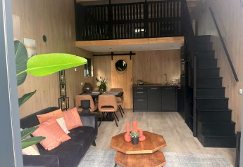 Hébergement glamping moderne avec salon, coin cuisine, mezzanine, salle à manger et décoration chaleureuse.