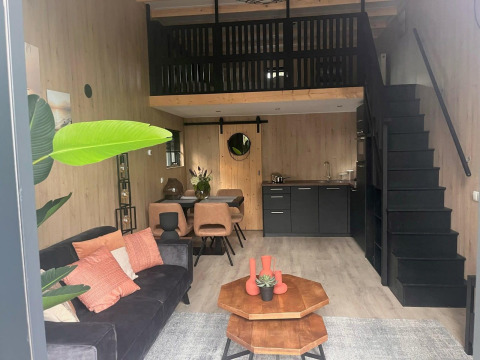Modern glamping accommodation featuring a cozy living area, kitchenette, loft bedroom, and dining space.