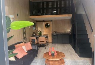 Modern glamping accommodation featuring a cozy living area, kitchenette, loft bedroom, and dining space.