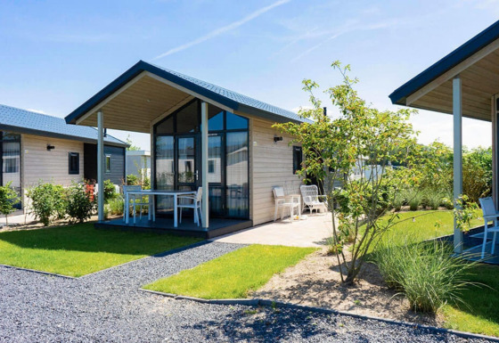 Photo of a modern Tiny House with large glass windows, porch, and garden on a sunny day.