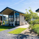 Billede af et moderne Tiny House med stor glasfacade, terrasse og have på solrig sommerdag.