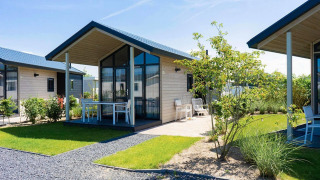 Billede af et moderne Tiny House med stor glasfacade, terrasse og have på solrig sommerdag.