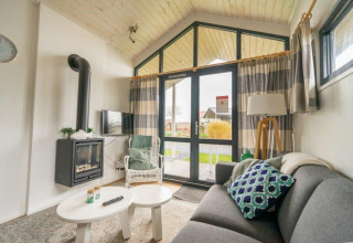 Acogedora sala de estar en Tiny House de EuroParcs Veluwemeer, Países Bajos, con chimenea y grandes ventanas.