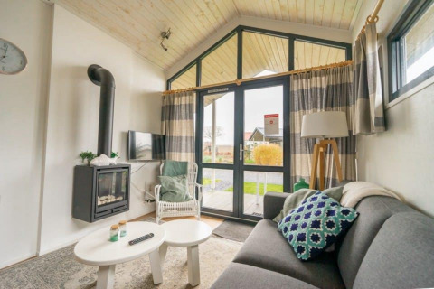 Salon confortable dans un Tiny House à EuroParcs Veluwemeer, Pays-Bas, avec cheminée et grandes fenêtres.