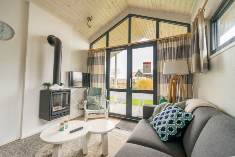 Acogedora sala de estar en Tiny House de EuroParcs Veluwemeer, Países Bajos, con chimenea y grandes ventanas.