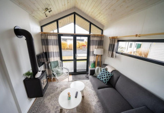 Acogedora sala de estar en una tiny house de EuroParcs Veluwemeer, con estufa y grandes ventanales.