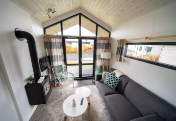 Salon d'une tiny house à EuroParcs Veluwemeer, aux Pays-Bas, avec poêle et grandes fenêtres lumineuses.
