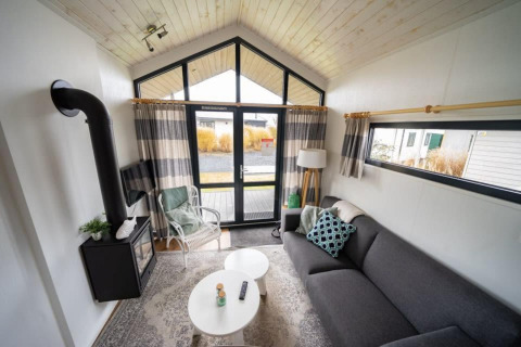 Stilfuld stue i et lille hus på EuroParcs Veluwemeer, med store vinduer, brændeovn og sofa.