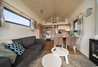 Interior de una tiny house en EuroParcs Veluwemeer, Países Bajos, con sofá, mesa de comedor y altillo.