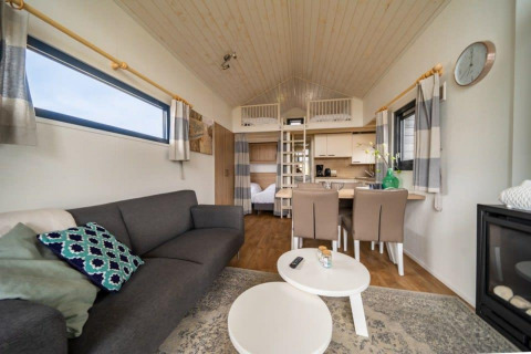 Interni di una tiny house a EuroParcs Veluwemeer, Paesi Bassi, con divano, tavolo da pranzo e soppalco.