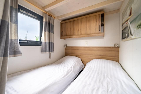 Two single beds with white linens in a tiny house at EuroParcs Veluwemeer, Netherlands, under wood cabinets.