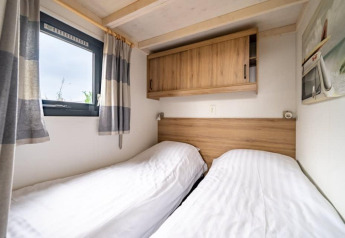 Deux lits simples avec draps blancs dans une tiny house à EuroParcs Veluwemeer, Pays-Bas, sous placard en bois.