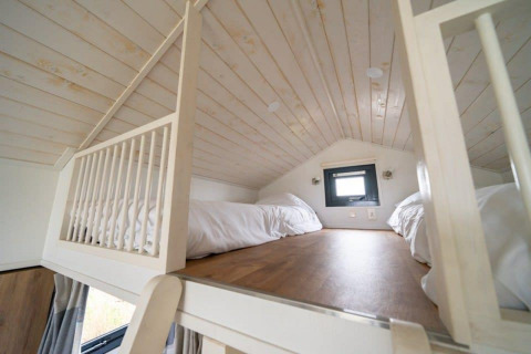 Dormitorio tipo loft con dos camas, techo de madera y ventana pequeña en Tiny House en EuroParcs Veluwemeer, Países Bajos.