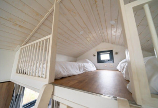 Dormitorio tipo loft con dos camas, techo de madera y ventana pequeña en Tiny House en EuroParcs Veluwemeer, Países Bajos.