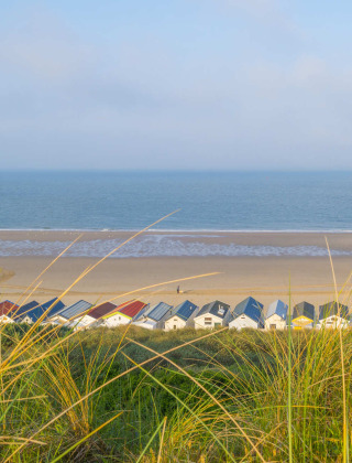 Blick auf den Strand von Westkapelle, Zeeland, Niederlande, mit bunten Strandhütten und Meer im Hintergrund.