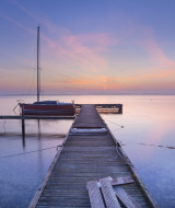 Holzsteg mit festgemachtem Boot im ruhigen Wasser bei Sonnenuntergang nahe Westkapelle, Zeeland, Niederlande.