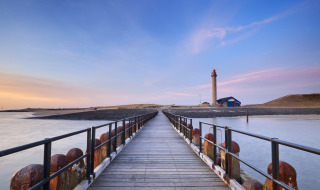 Langer Steg führt zu einem Leuchtturm nahe Westkapelle in Zeeland, Niederlande, im sanften Abendlicht.