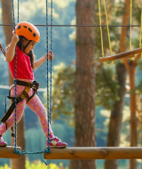 Niña con casco y arnés cruza un circuito de cuerdas en el bosque cerca de Malgrat de Mar, Barcelona, Cataluña.
