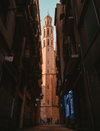Callejón estrecho en Malgrat de Mar, Barcelona, enmarcando una torre histórica iluminada al atardecer.