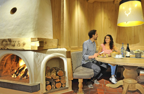 Couple enjoys a cozy meal by the fireplace at Camping Seeblick Toni holiday park in Tirol, Austria, warm lighting.