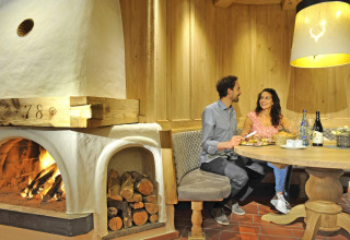Couple enjoys a cozy meal by the fireplace at Camping Seeblick Toni holiday park in Tirol, Austria, warm lighting.