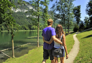Koppel wandelt langs een meer met bergen en bomen bij Camping Seeblick Toni in Tirol, Oostenrijk.