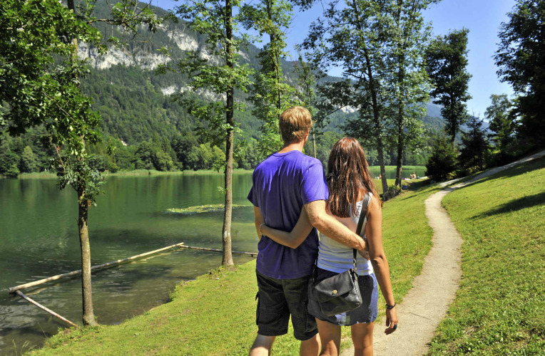 Paar spaziert am See entlang, umgeben von Bergen und Bäumen, im Camping Seeblick Toni, Tirol, Österreich.