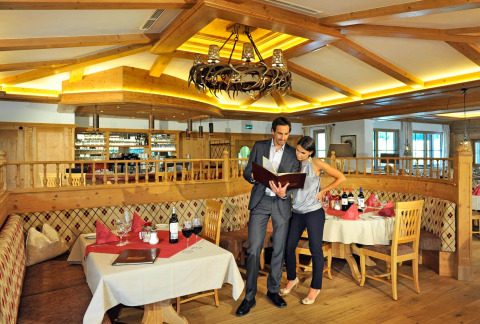 Pareja leyendo el menú en un restaurante acogedor de Camping Seeblick Toni, Tirol, Austria. Decoración rústica.