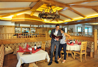 Couple browsing the menu at a cozy restaurant in Camping Seeblick Toni, Tirol, Austria. Warm wooden décor.