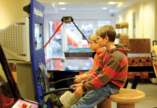 Two boys playing an arcade game in the recreation room at Camping Seeblick Toni holiday park in Austria.