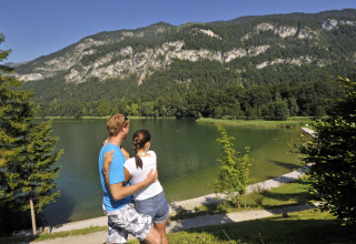 Una pareja disfruta la vista de un lago y montañas en Camping Seeblick Toni, un parque vacacional en Tirol, Austria.