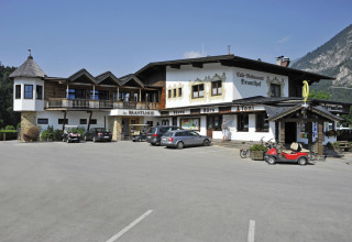 Camping Seeblick Toni vakantiepark in Tirol, Oostenrijk, met restaurant, geparkeerde auto's en bergen op de achtergrond.