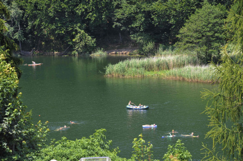 People swimming and boating on a lush green lake surrounded by trees at Camping Seeblick Toni in Tyrol, Austria.