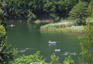 Menschen schwimmen und fahren mit Booten auf einem See, umgeben von Bäumen bei Camping Seeblick Toni, Tirol.