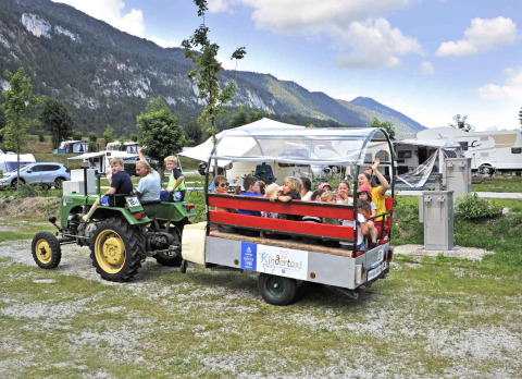Niños disfrutan de un paseo en tractor en Camping Seeblick Toni, Tirol, Austria, con montañas y caravanas.