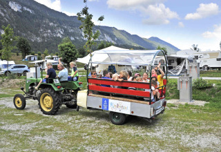 Børn nyder en traktortur på Camping Seeblick Toni i Tirol, Østrig, omgivet af bjerge og campingvogne.