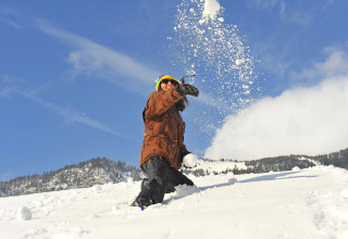 Persoon gooit een sneeuwbal op Camping Seeblick Toni in Tirol, Oostenrijk, met bergen op de achtergrond.