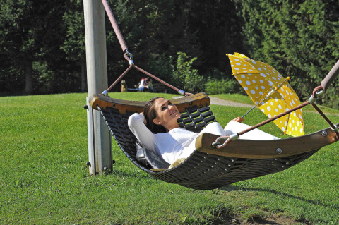 Vrouw relaxt in een hangmat met gele paraplu bij Camping Seeblick Toni in Tirol, Oostenrijk, omgeven door natuur.