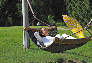 Donna che si rilassa sull'amaca con ombrello giallo al Camping Seeblick Toni in Tirolo, Austria, immersa nella natura.