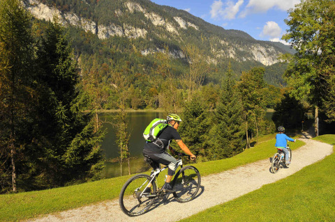 Twee mensen fietsen op een pad naast een meer met bergen bij Camping Seeblick Toni in Tirol, Oostenrijk.