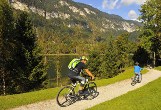 Twee mensen fietsen op een pad naast een meer met bergen bij Camping Seeblick Toni in Tirol, Oostenrijk.