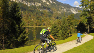 Dos personas en bicicleta por un sendero junto a un lago y montañas en Camping Seeblick Toni, Tirol, Austria.