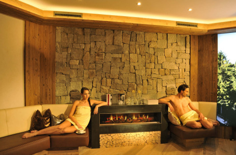 Zona wellness relajante con dos huéspedes junto a la chimenea en Camping Seeblick Toni, Tirol, Austria.