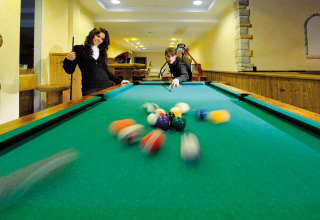 Two people play billiards at Camping Seeblick Toni holiday park in Tirol, Austria. Balls scatter on table.