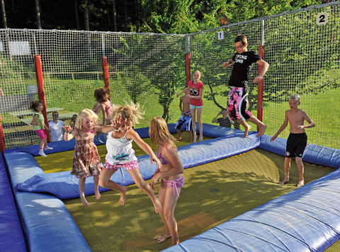 Niños y adultos saltando juntos en una gran cama elástica en Camping Seeblick Toni en Tirol, Austria, durante el día.
