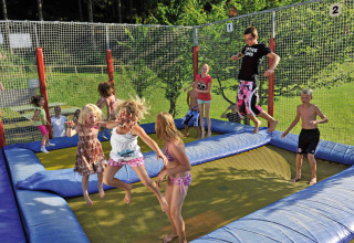 Børn og voksne hopper sammen på en stor trampolin i Camping Seeblick Toni i Tirol, Østrig, på en solskinsdag.