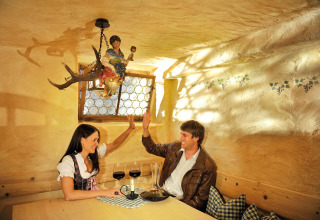 Ein lächelndes Paar in Tracht gibt sich im Restaurant von Camping Seeblick Toni in Tirol, Österreich, ein High-Five.