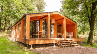 Cabaña Forresthouse Scandi de madera moderna con porche cubierta, ubicada en un claro soleado del bosque.