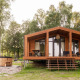 Træhytte kaldet Lakehouse med hottub foran og terrasse, omgivet af grønne træer og natur.