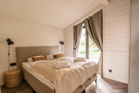 Acogedor dormitorio luminoso con cama doble, ventanales y cortinas en Lakehouse + Hottub, Wilsumer Berge, Alemania.